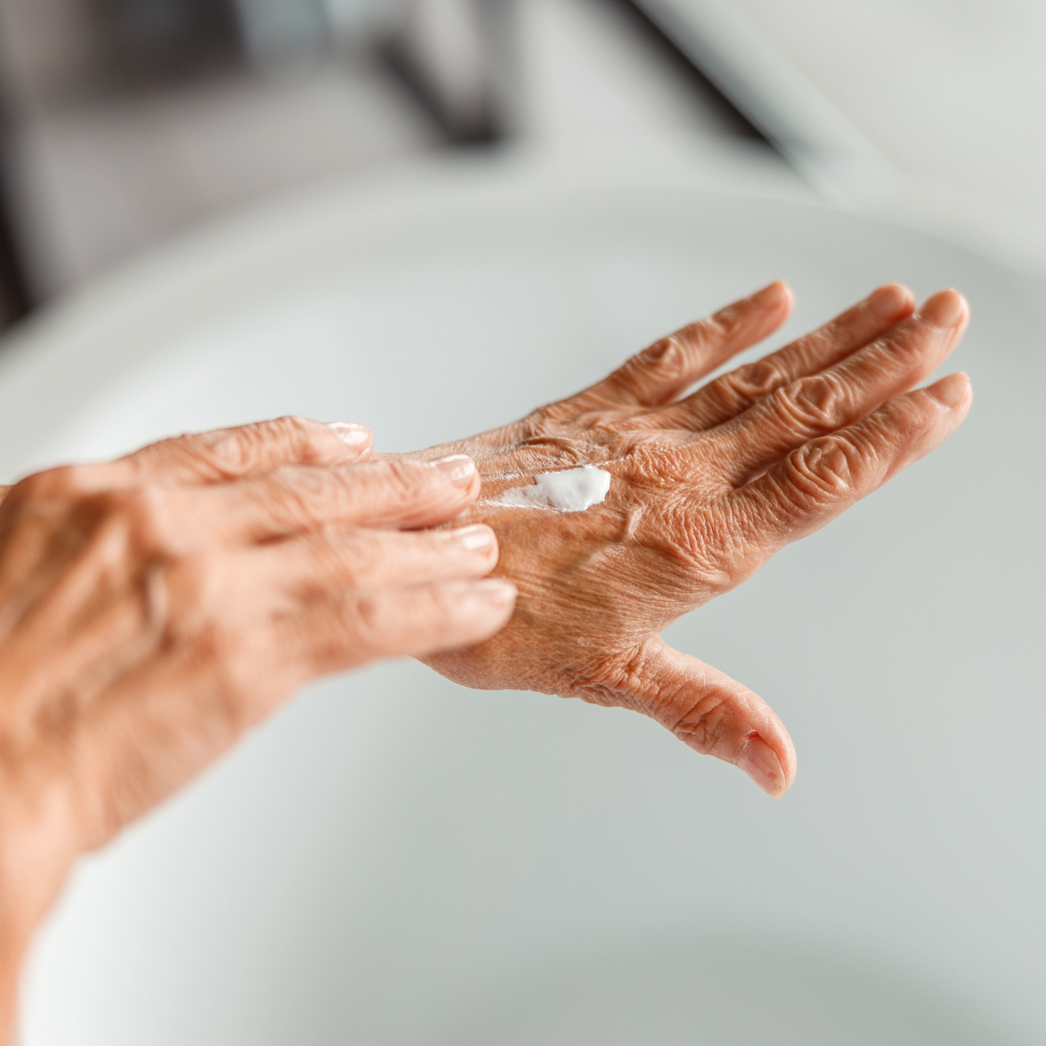 Starejša ženska nanaša vlažilno polžjo kremo na roke — Heliroyal Plus naravna nega za zrelo kožo in zmanjšanje gub. Krema za suho kožo z anti-age učinkom.